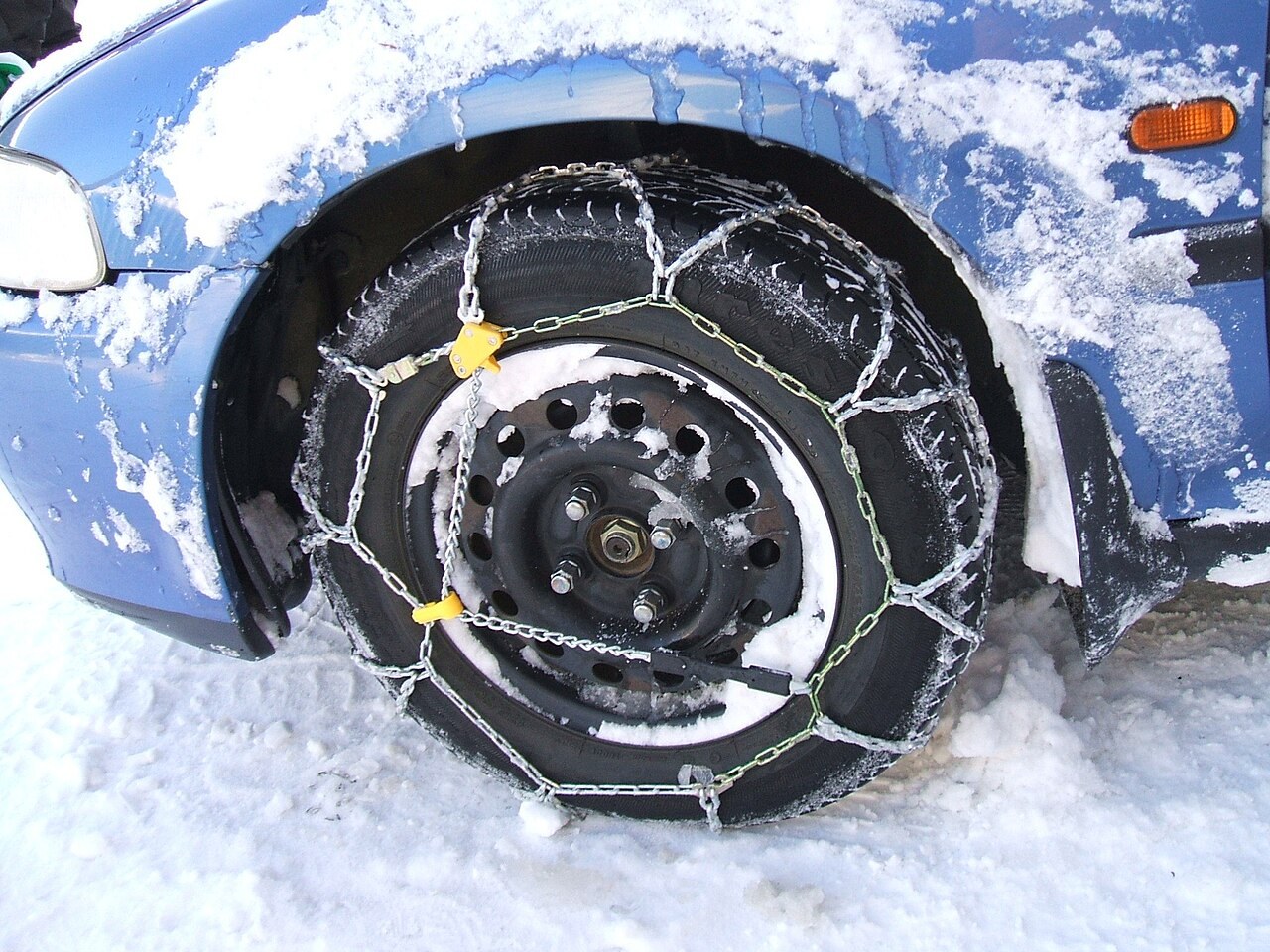Snow chain within the wheel arch of a snow-covered car